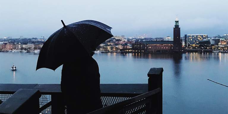 A person with an umbrella is looking at Stockholm City Hall on a rainy evening.