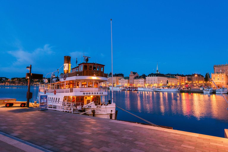 En ångbåt i vattnet utanför Stockholms Slott i Gamla Stan. Kväll. I bakgrunden syns Gamla Stan.