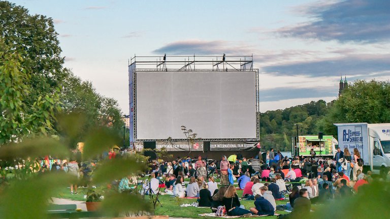 Kultur i Stockholm. En stor grupp med människor, samlad för att titta på utomhusbio i Rålambshovsparken.