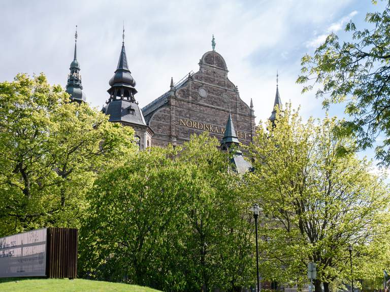 Museer i Stockholm. Nordiska museet på Djurgården, exteriör. Bilden är tagen under en solig vårdag, med grönskande träd framför museet.