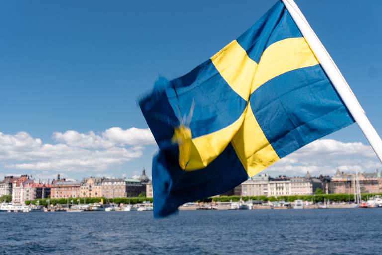 Sommar i Stockholm. En svensk flagga svajjar i vinden. Bortom den i horisonten syns Östermalm.