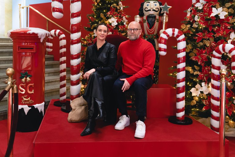 Sofie von Reis och Joakim Petterson. Julskyltning på NK. 2023. En kvinna och man sitter omgivna av färgglatt julpynt.