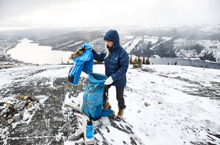 En person som packar sin ryggsäck utomhus i de snöiga bergen.