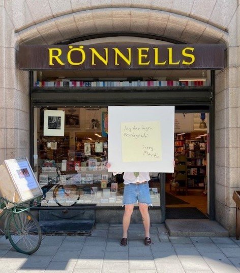En person står utanför bokhandeln Rönnells och håller upp ett stort skivomslag.