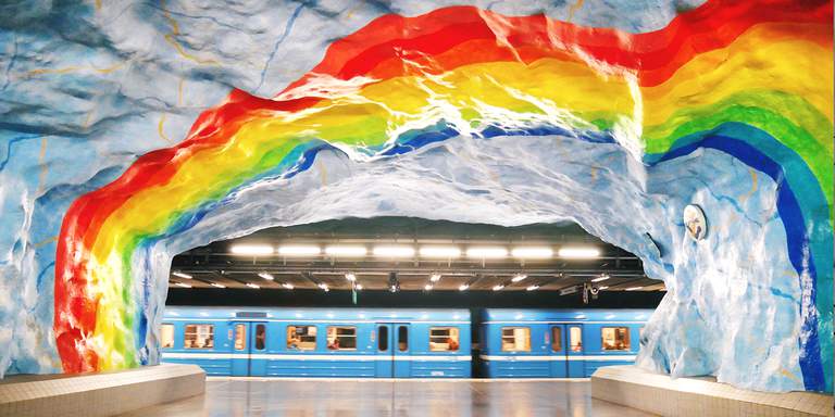 Stadions tunnelbanestation, perrong. På bilden syns ett grottvalv, målat i ljusblått med en regnbåge. I bakgrunden ankommer precis en tunnelbana till stationen.