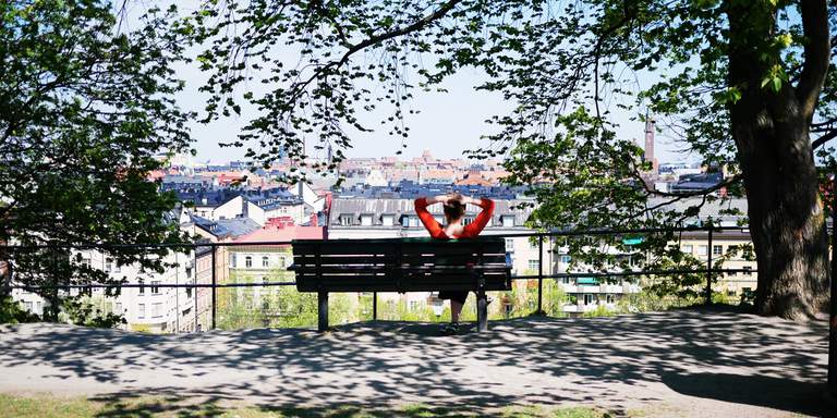 Parker i Stockholm. En ung kvinna sitter på en parkbänk och beundrar utsikten från observatorielunden i centrala Stockholm. Det är en solig dag och stora delar av norra innerstan är synliga från utsiktsplatsen.