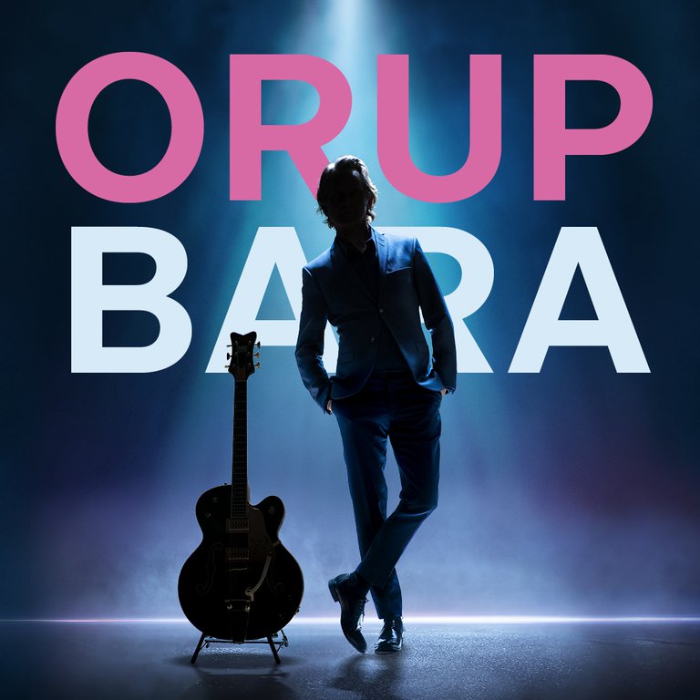 En musiker med en gitarr bredvid sig och texten bakom sig "Orup bara".