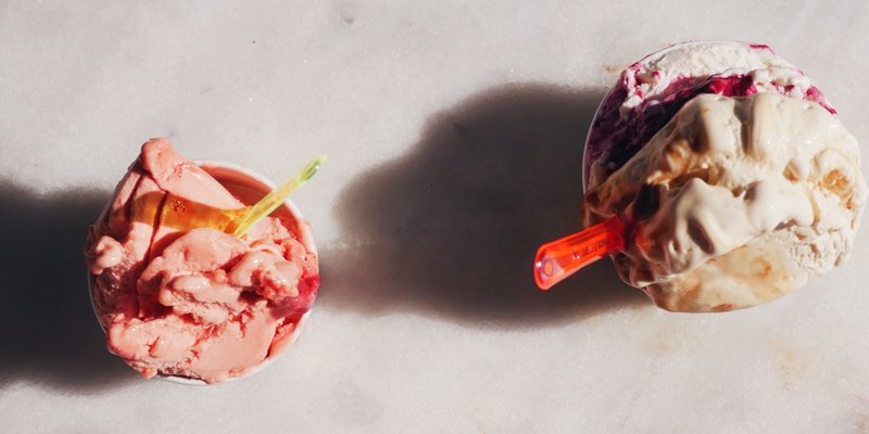 Two paper cups, filled with two different flavors of ice cream.