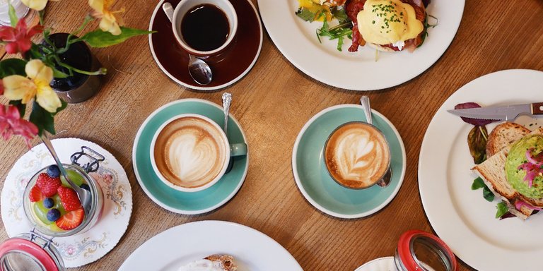 Brunch på Greasy Spoon i Stockholm med cappuccino, ägg benedict, avokadomacka och färska bär på ett träbord.