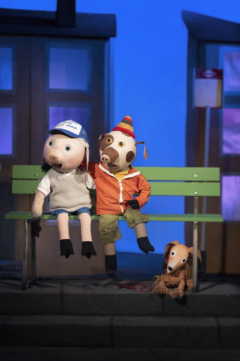 Tre muppdockor som föreställer två grisar som sitter på en bänk och en hund nära bänken.