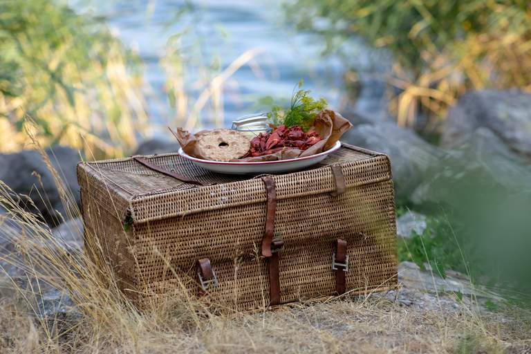 En tallrik med kräftor och knäckebröd på en picknickkorg på en strand nära vatten.
