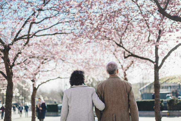 Vår i Stockholm. Ett medelålderspar, med ryggarna vända mot kameran, tar en promenad i Kungsträdgården. Det är en solig vårdag och i bakgrunden syns körsbärsträden blomma.