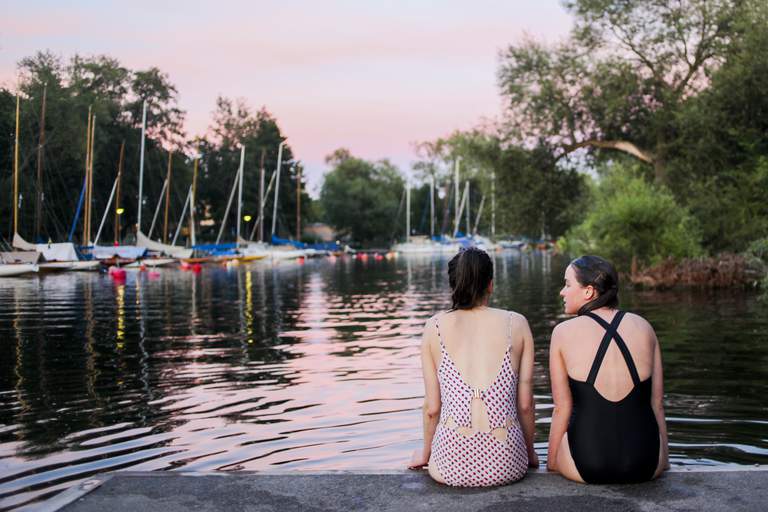 Två unga kvinnor i baddräkt sitter vid vattnet på Långholmen efter ett bad. Det finns många bra badställen i Stockholmstrakten, även i centrala Stockholm.