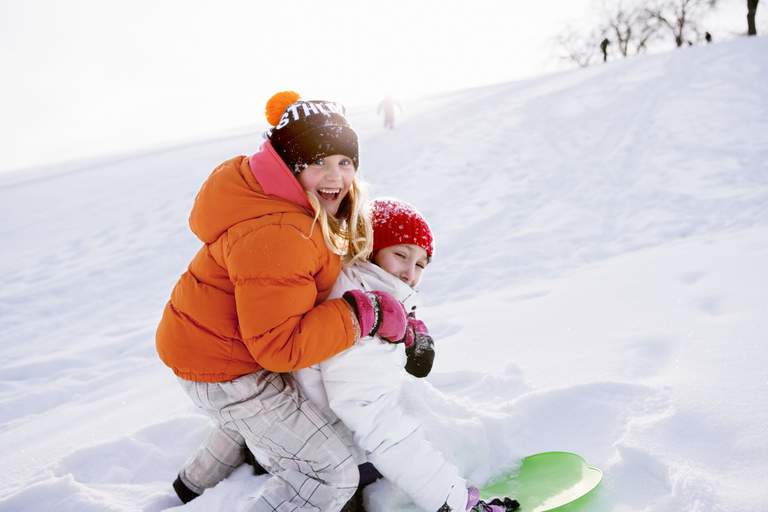 Två barn som åker pulka i en snöig backe i Stockholm