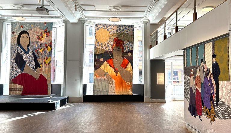 Museer i Stockholm. Forum för levande historia i Gamla stan. Stora tavlor, på kvinnor i traditionella kläder, hänger på museets väggar.