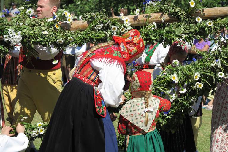 Människor i svenska folkdräkter reser en majstång.