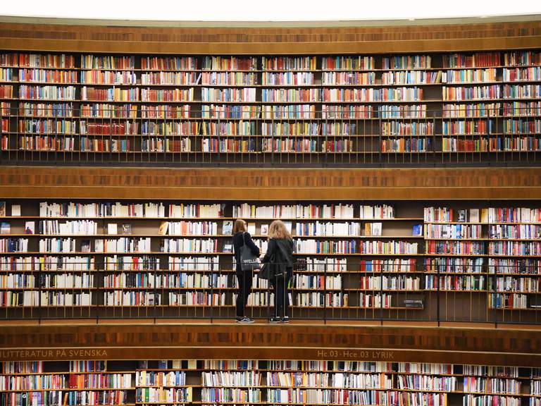 Kultur i Stockholm. Stadsbiblioteket, interiör. Två kvinnor står framför hyllor fulla av böcker.