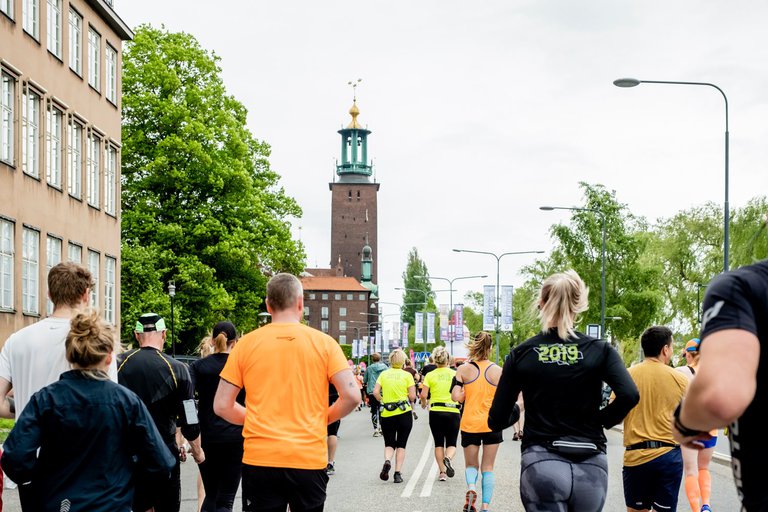 En grupp människor springer på en Stockholmsgata med Stockholms Stadshus i bakgrunden