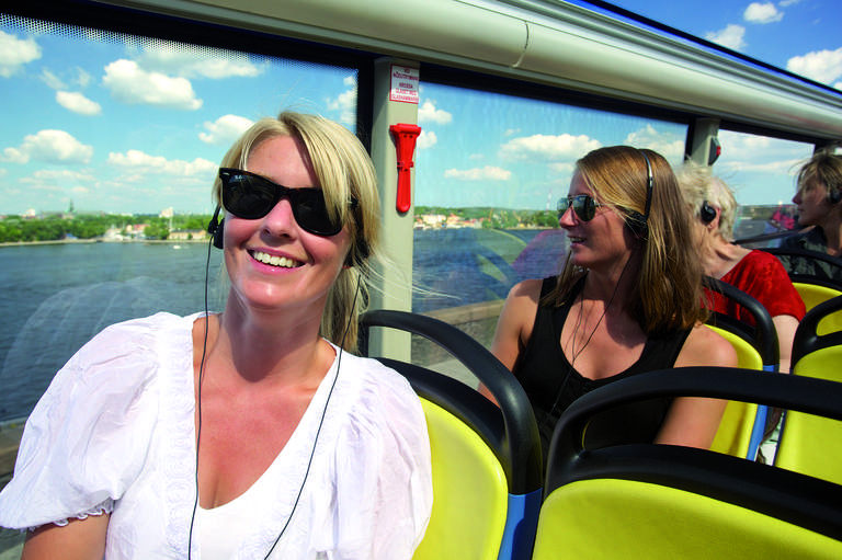 Turister på Hop-On Hop-off-buss som lyssnar på en audioguidad tur.