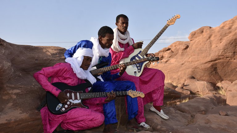 Musikerna som sitter med sina gitarrer utomhus.