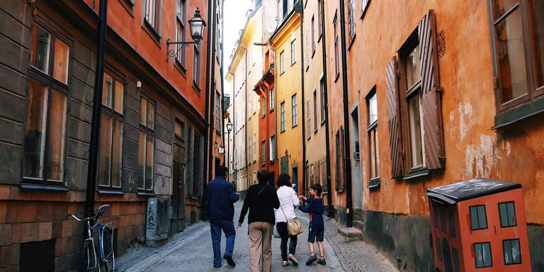 A group of visitors are walking, looking happy on the cobbled streets of Gamla Stan. Prästgatan is one of the prettiest, lined by beautiful coloured houses in terracotta hues.
