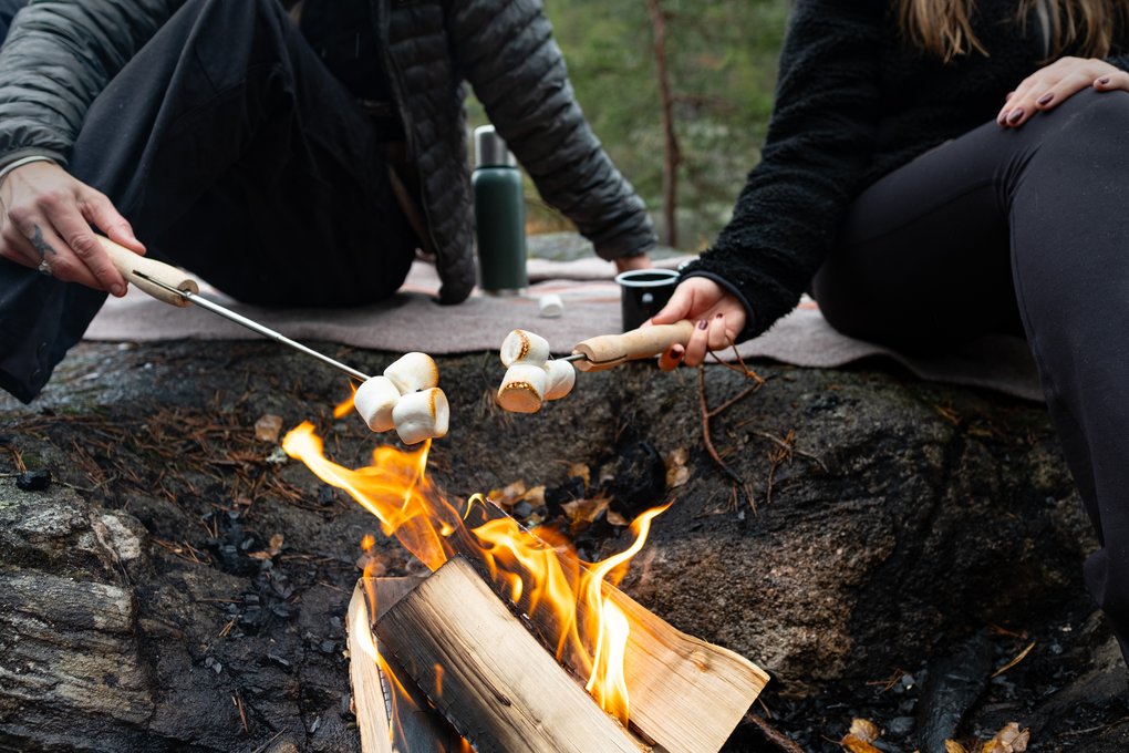 Två personer grillar marshmallows över en eld i en uteplatsmiljö.