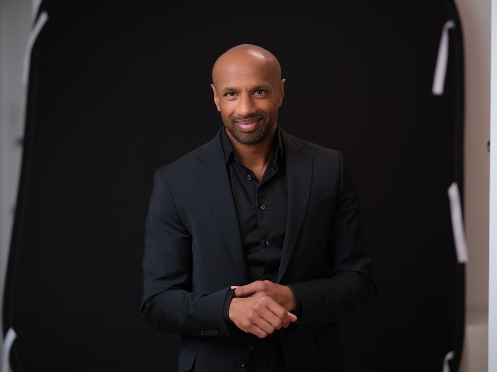 En man i svart skjorta och kavaj mot svart bakgrund.