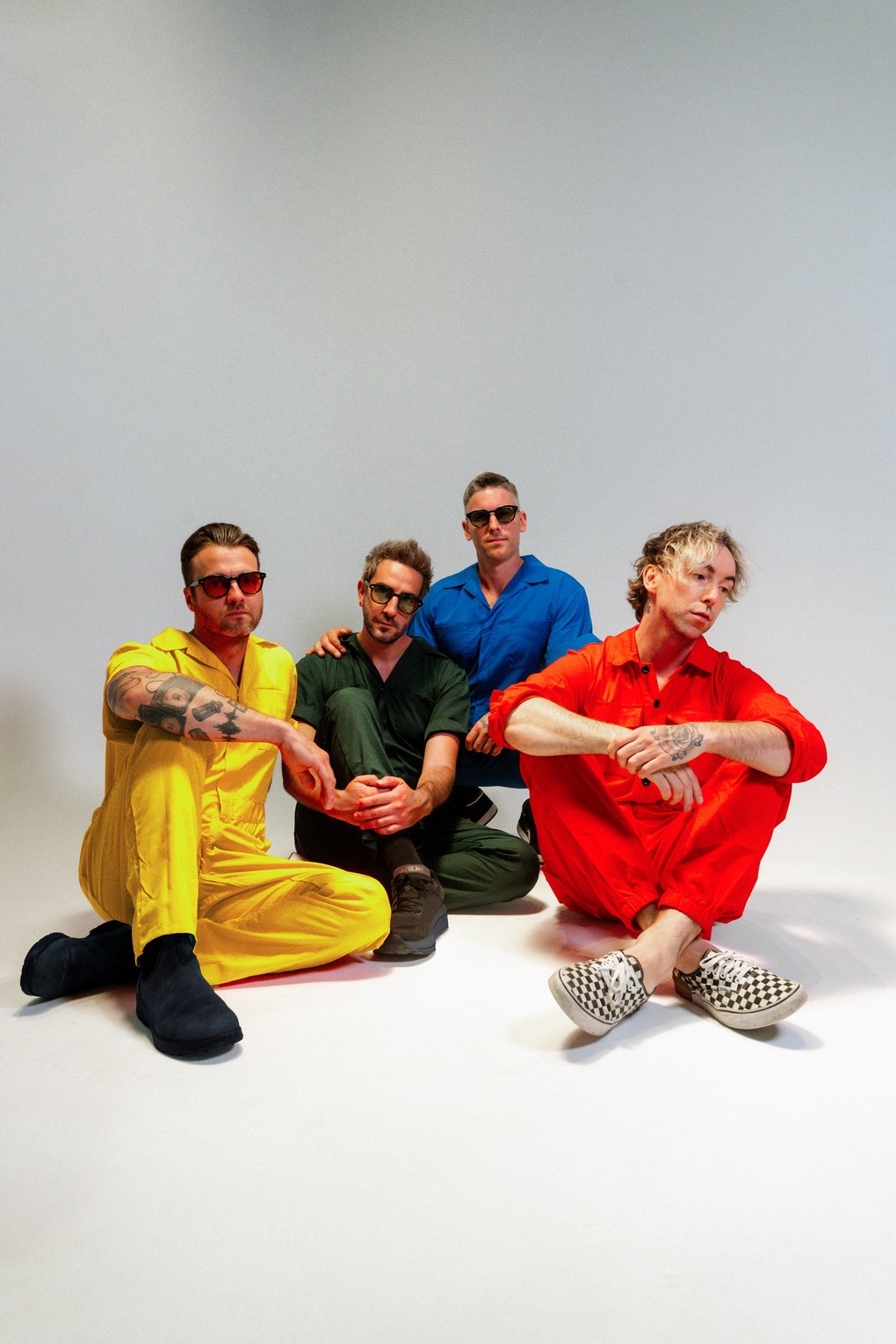 Medlemmarna i All Time Low sitter på golvet, iklädda overaller i starka färger.