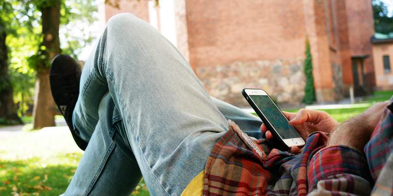 En man ligger på en gräsmatta och tittar på sin mobiltelefonen. På skärmen syns en kartapp.