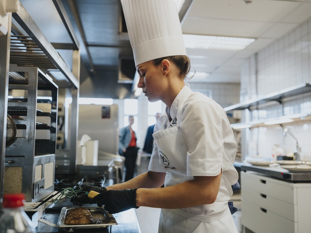 Kock i professionellt kök som kontrollerar temperaturen på kött.