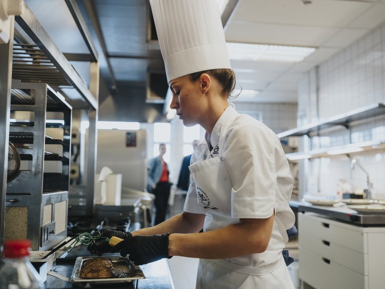Kock i professionellt kök som kontrollerar temperaturen på kött.
