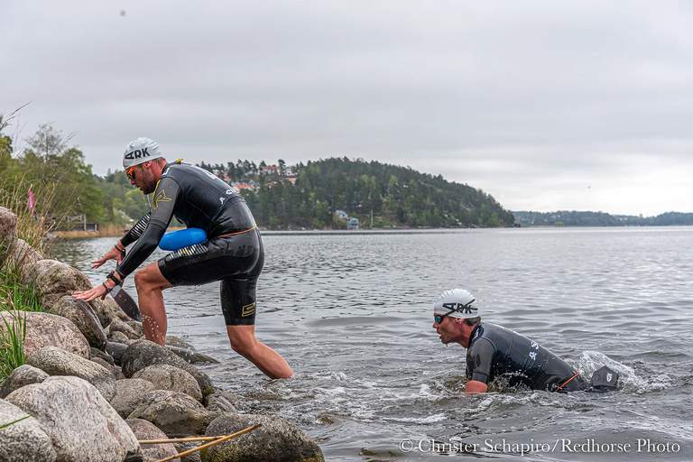 Två simmare kommer ut från vattnet till stranden.