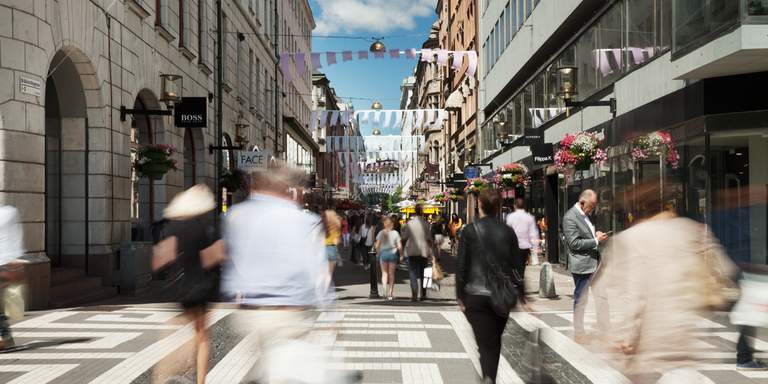 Vår i Stockholm. Människor, i rörelseoskärpa, går förbi kameran på Biblioteksgatan. I bakgrunden syns några av stadsdelens alla exklusiva märkesbutiker.