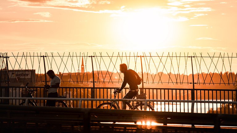 Cykla i Stockholm. En man cyklar längs med Västerbron i Solnedgången.