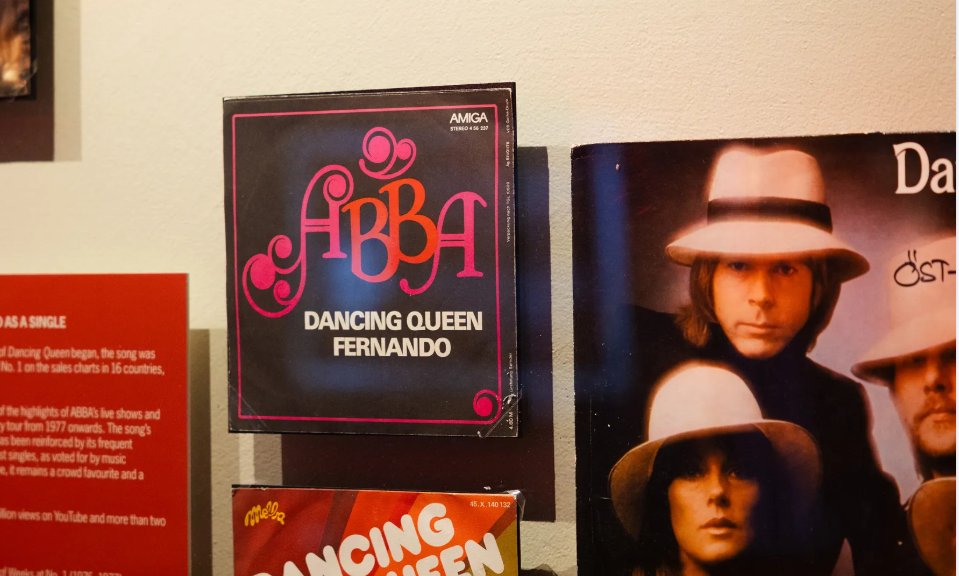 Bilden visar en vinylskiva och en CD-hylle med ABBA:s låt Dancing Queen samt en annan skivomslag med en man i hatt. Skivorna är placerade på en hylla med informationstext bredvid.