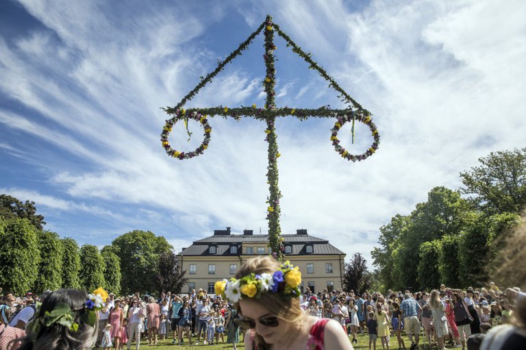 Folk som dansar runt midsommarstång.