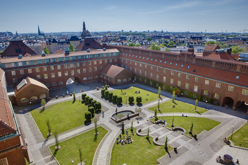 Flygvy över KTH:s borggård med röda tegelbyggnader, grön gård och människor som njuter i solen.