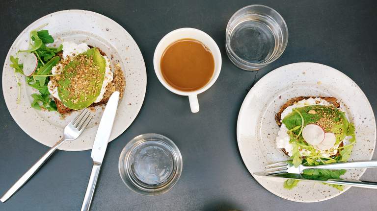 Frukost i Stockholm. Ett bord är dukat med två avocadomackor, kaffe och glas med vatten