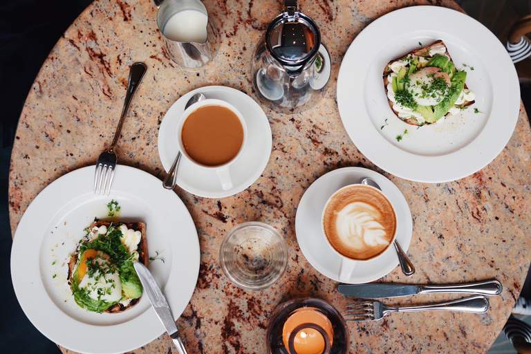 Två avocadomackor med pocherade ägg på samt två kaffekoppar på ett rosa marmorbord