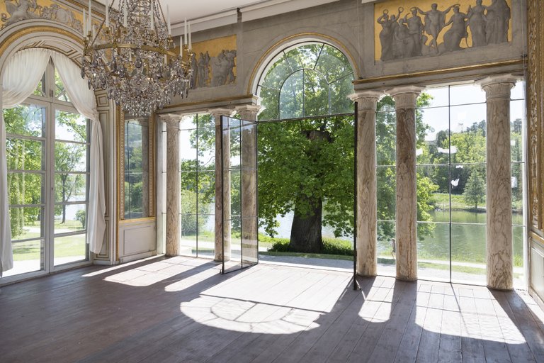 En del av paviljongen med kristallkronor och pelare, som öppnar upp mot en vacker utsikt över grönskande träd.