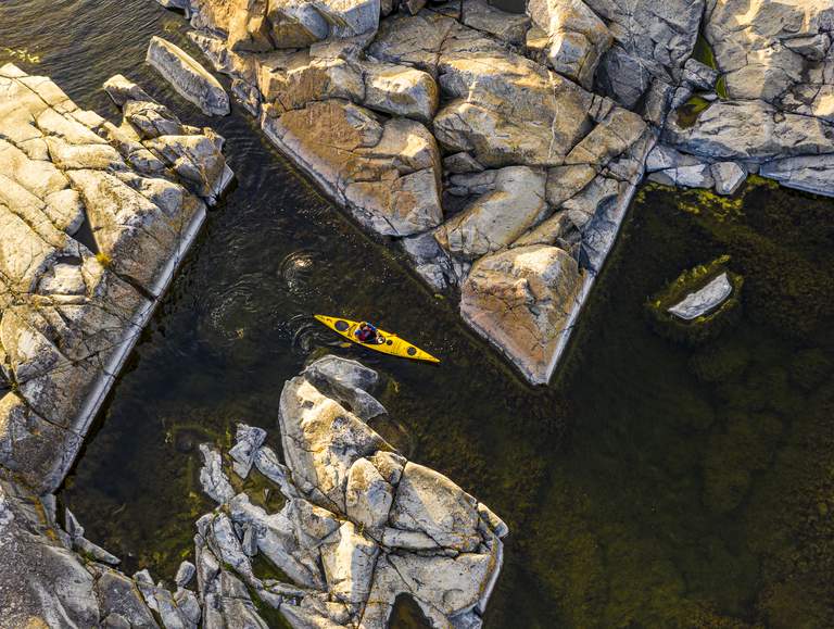 Äventyr i Stockholms skärgård. Fågeperspektiv på en kanot som navigerar genom skär i Stockholms skärgård.