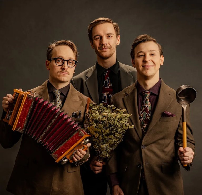 Humor- och musikgruppen KAJ klädd i bruna kostymer och med traditionella bastutillbehör och ett litet dragspel.