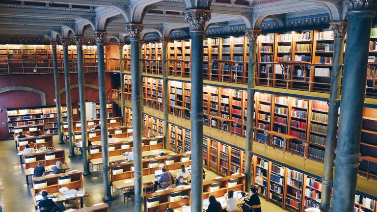 Sevärdheter i Stockholm. Kungliga biblioteket. Människor sitter i stora läsesalen vid långa bord.