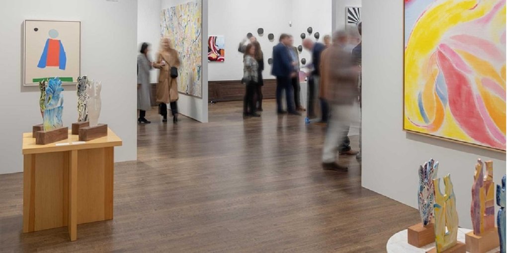 Utställningshall med målningar, skulpturer och besökare.