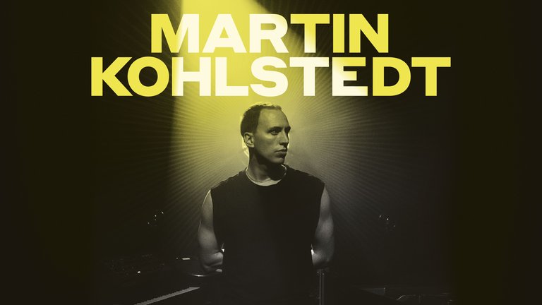 En muskulös man i svart linne upplyst bakifrån av en grön spotlight.