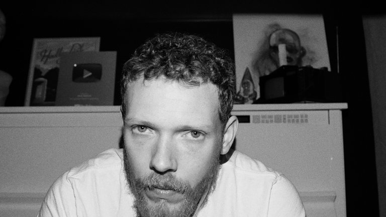 En blond man framför ett vitt piano.