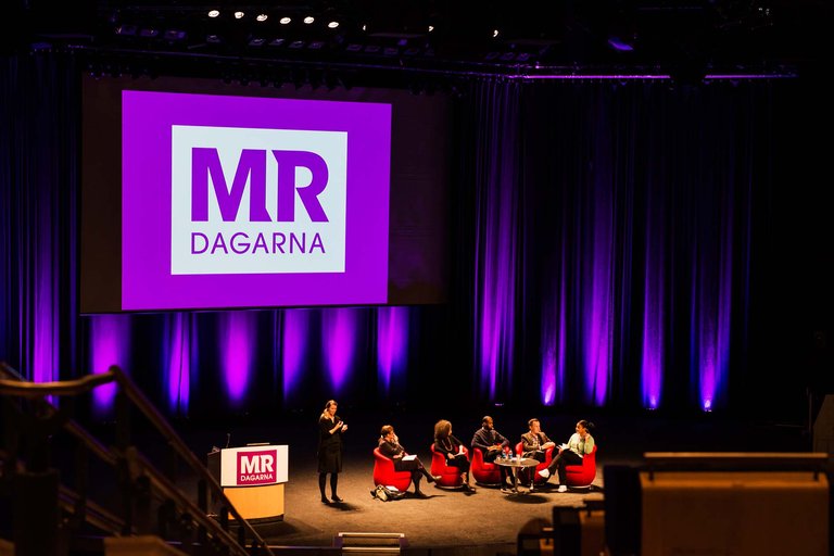 Panel discussion on stage at MR-dagarna, large logo screen and purple lighting.