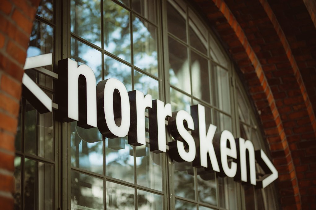Närbild på skylten ”<norrsken>” på en byggnad med glasfönster och tegelbågar.