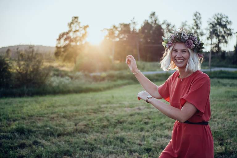 Midsommar i Stockholm. En kvinna dansar skrattandes på en äng. Solnedgång.