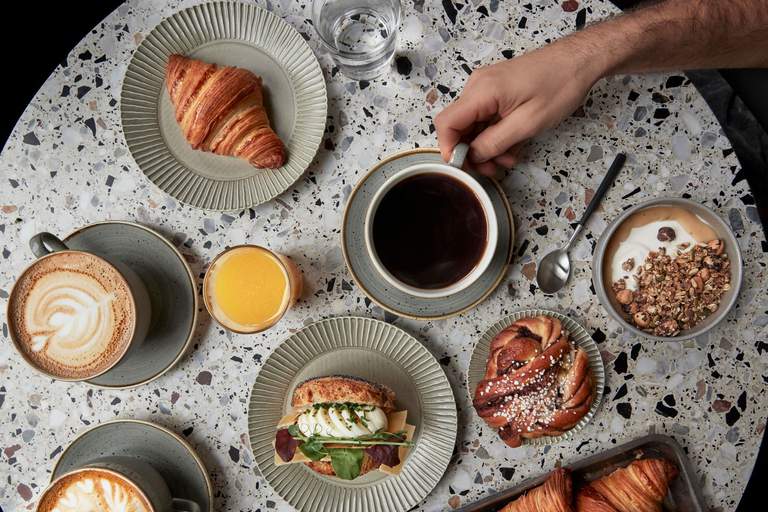 Kaféer i Stockholm. Ett bord dukar för fika på Komet i Stockholm. Kaffe, smörgås, kanelbulle med mera.